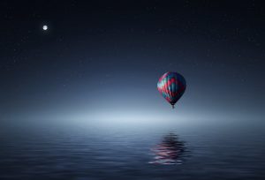 Dreamy image of hot air balloon floating above water in the night sky