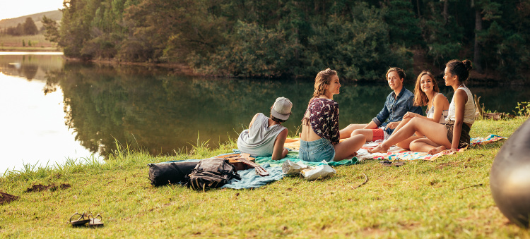 A group of young people on blankets relaxing near a lake