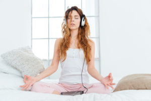 Woman meditating on bed with headphones on