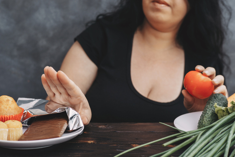 Overweight woman pushing away snacks in favor of vegetables